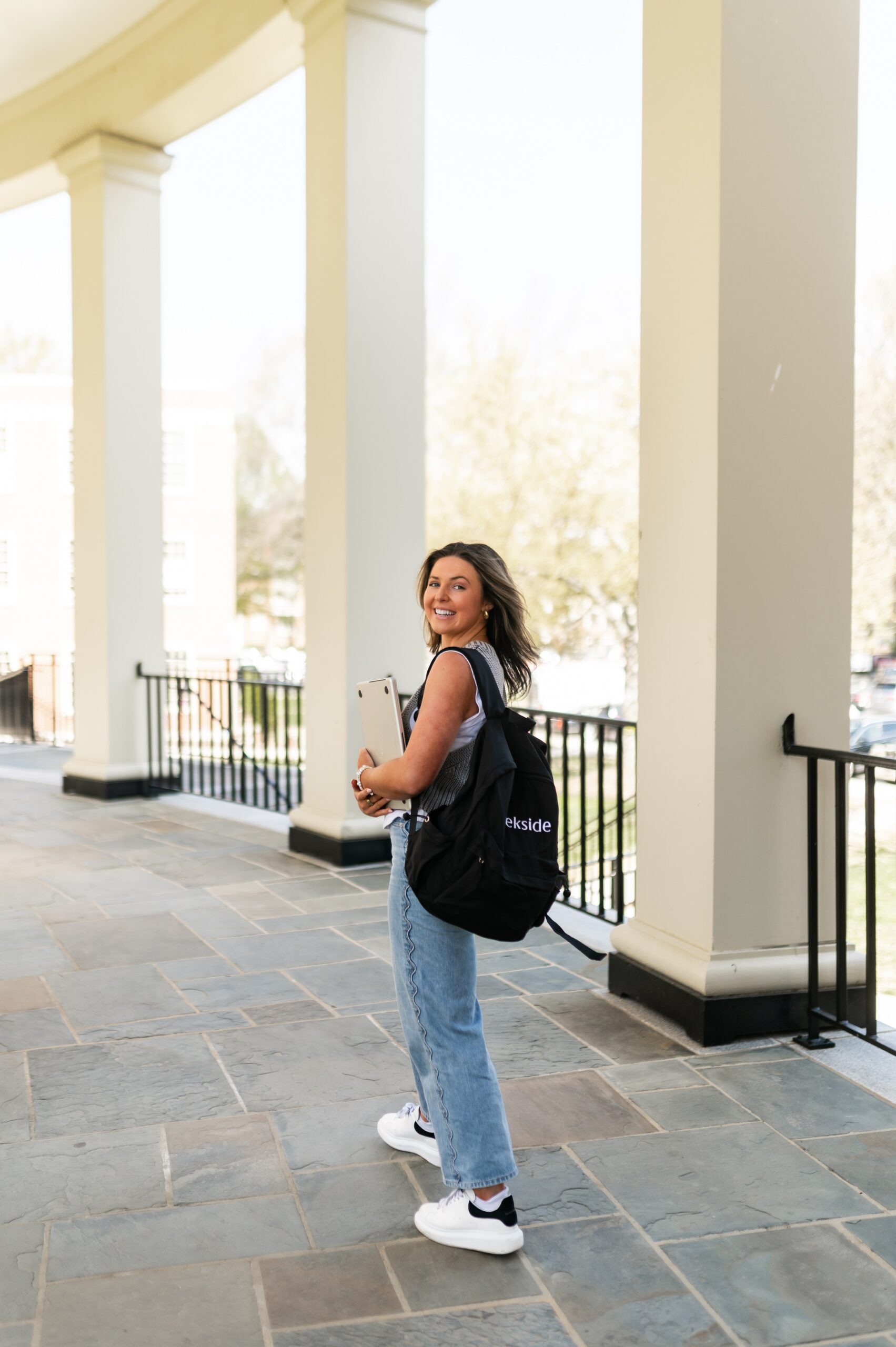 student carrying laptop past campus pillars scaled
