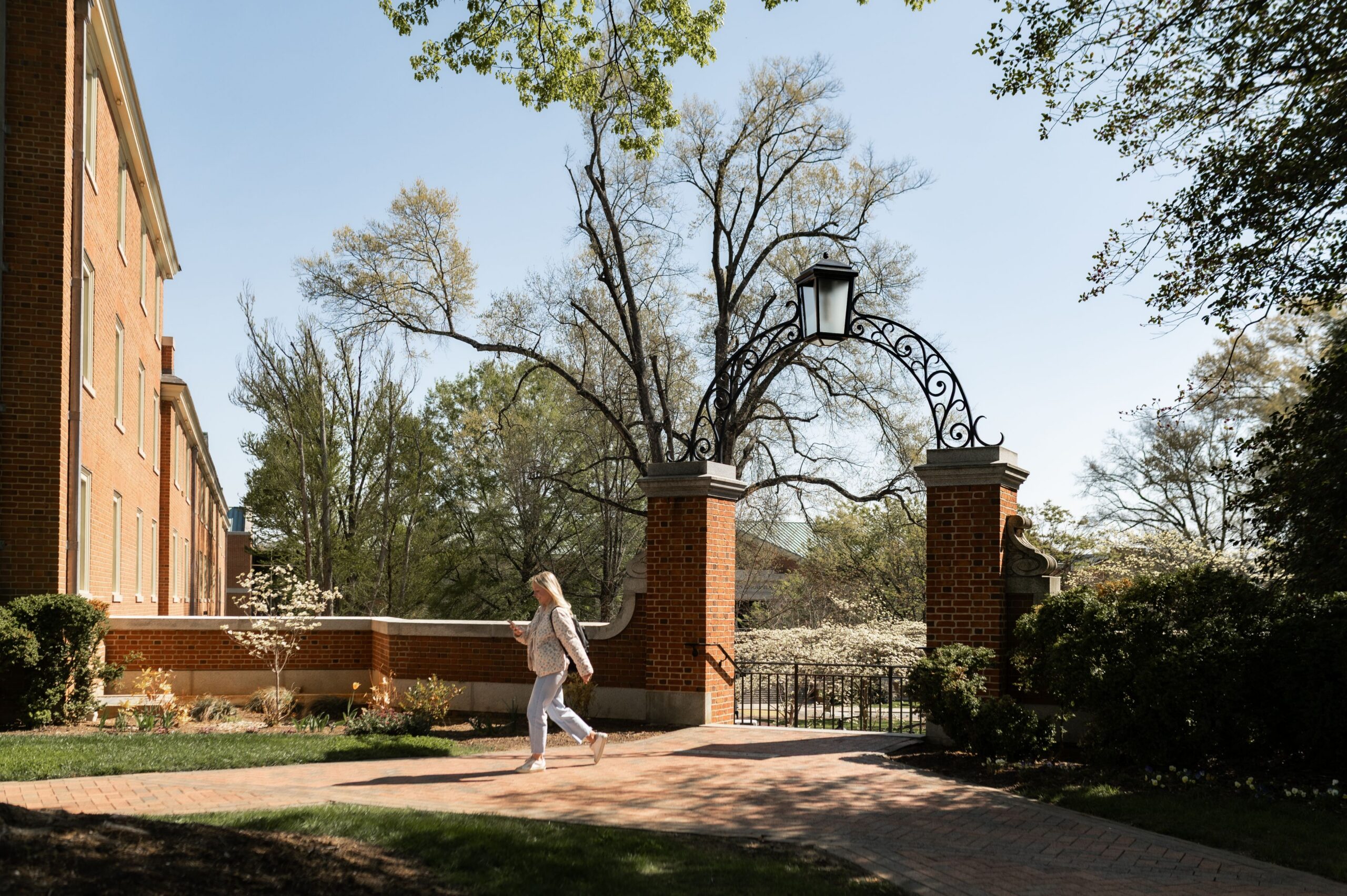 student walking past brick campus gateway scaled